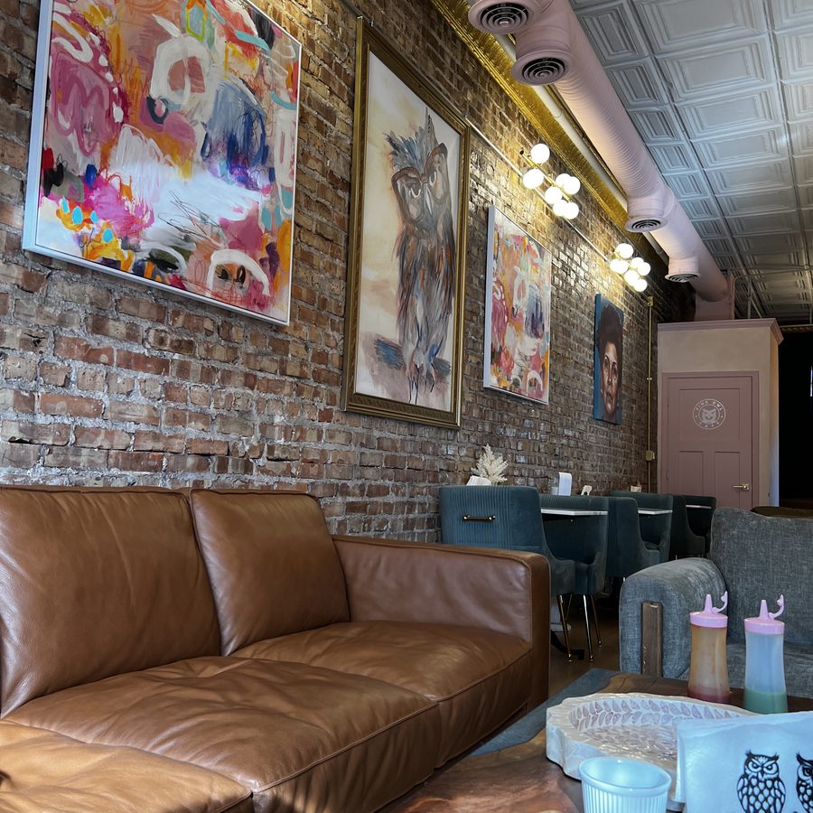 Paintings on the exposed brick, an owl among them, above the tan leather sofa